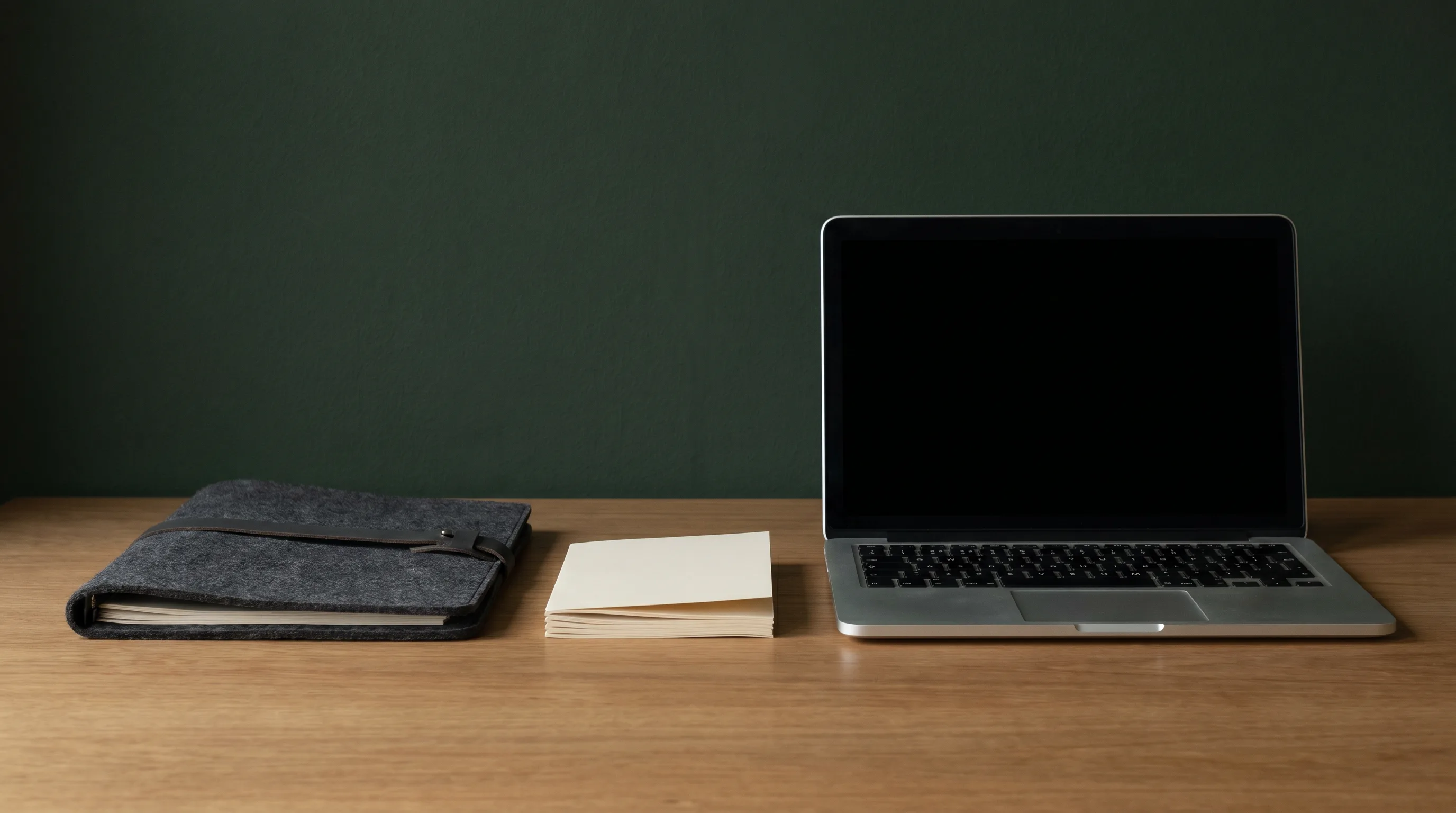 A closed felt document folder, a face-down stack of papers, and a laptop with a blank screen on a clean desk